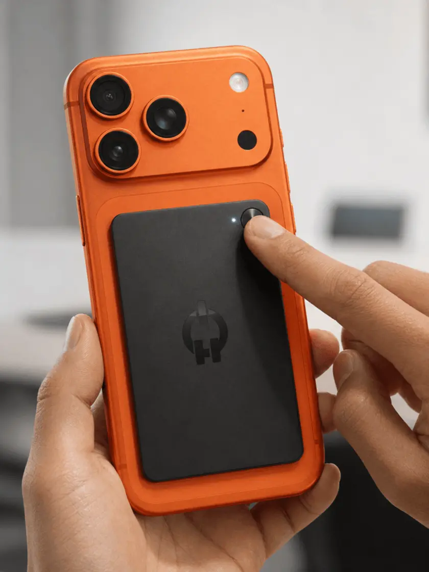 A thumb pressing the button on a Ruune attached to the back of an orange iPhone.